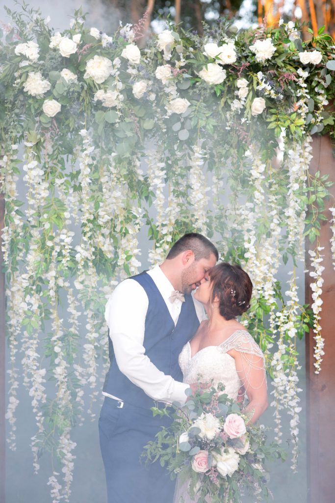 bride and groom with a wall of flowers on their wedding day