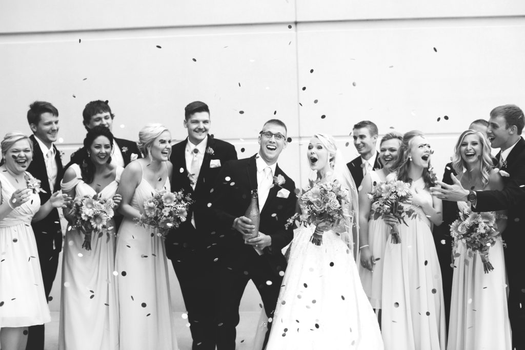 a wedding party popping confetti with the bride and groom
